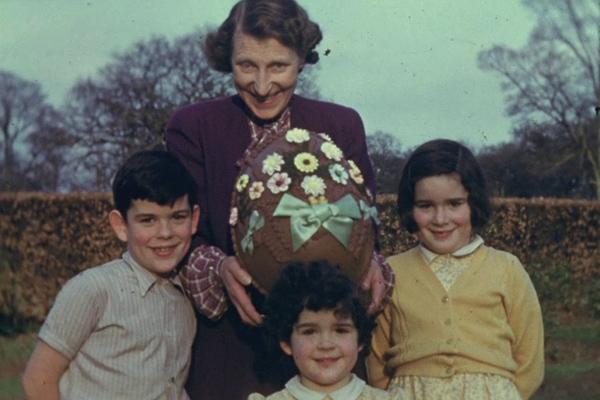 A colour still image from a home movie showing a family group with a huge Easter egg.
