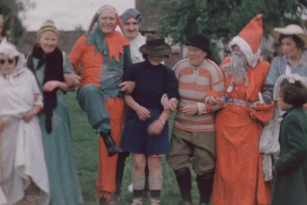 A colour still image from Coronation Festivities in Herefordshire (1953) showing a group of adults in fancy dress.