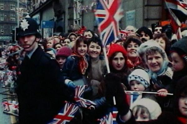 Image of a crowd waving Union Jacks, and a policeman standing by.