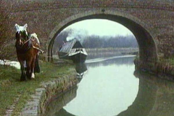 Image of a canal boat going under a small bridge.